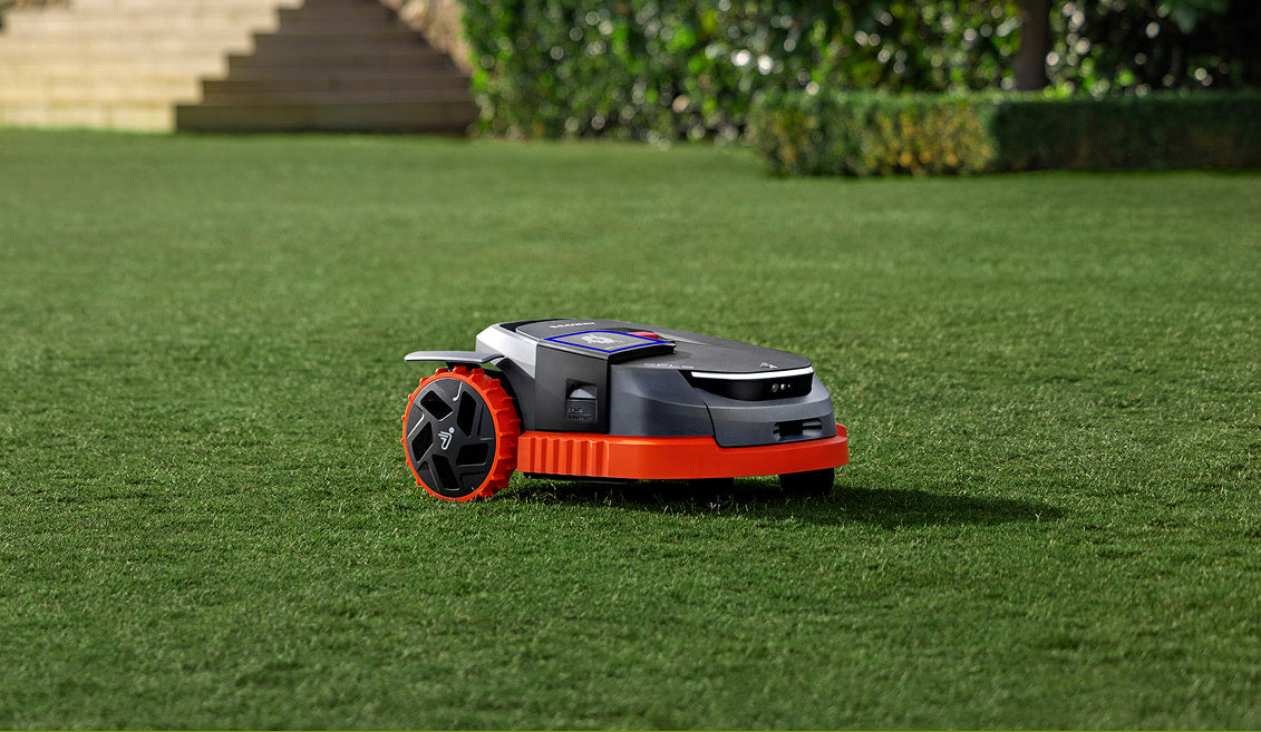 Navimow X3 Series robotic mower with orange wheels on a manicured lawn next to stone garden steps